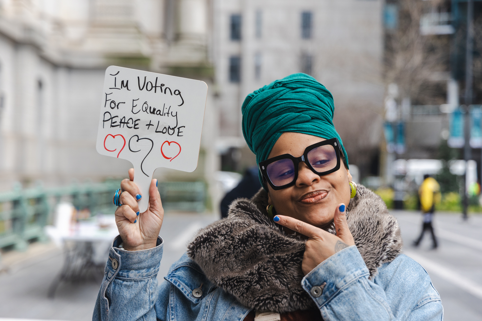 A woman on a city street holds up a handmade sign reading "I'm Voting For Equality"